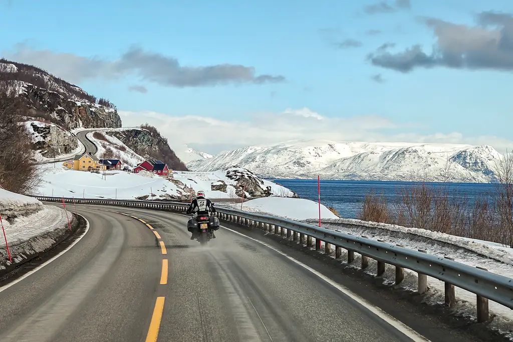 Motorcycle navigating snowy yet sunny roads beside a frozen lake in northern Norway, showcasing the Bridgestone T33’s grip and versatility.