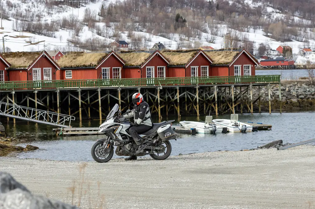Rider on the E6 along fjords and red wooden houses, tackling sudden snowstorm with Bridgestone T33 tyres on the Versys 1100.