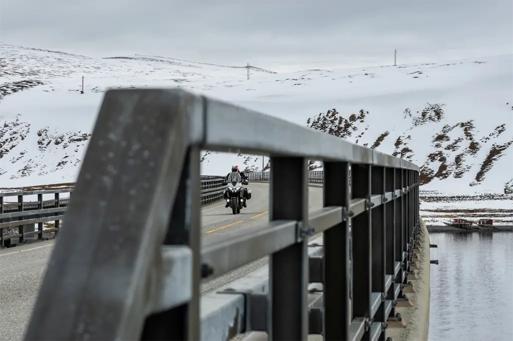 Motorcycle riding on Norway’s E69 toward the North Cape, showcasing Bridgestone T33 tyres handling cold, winding fjord roads.