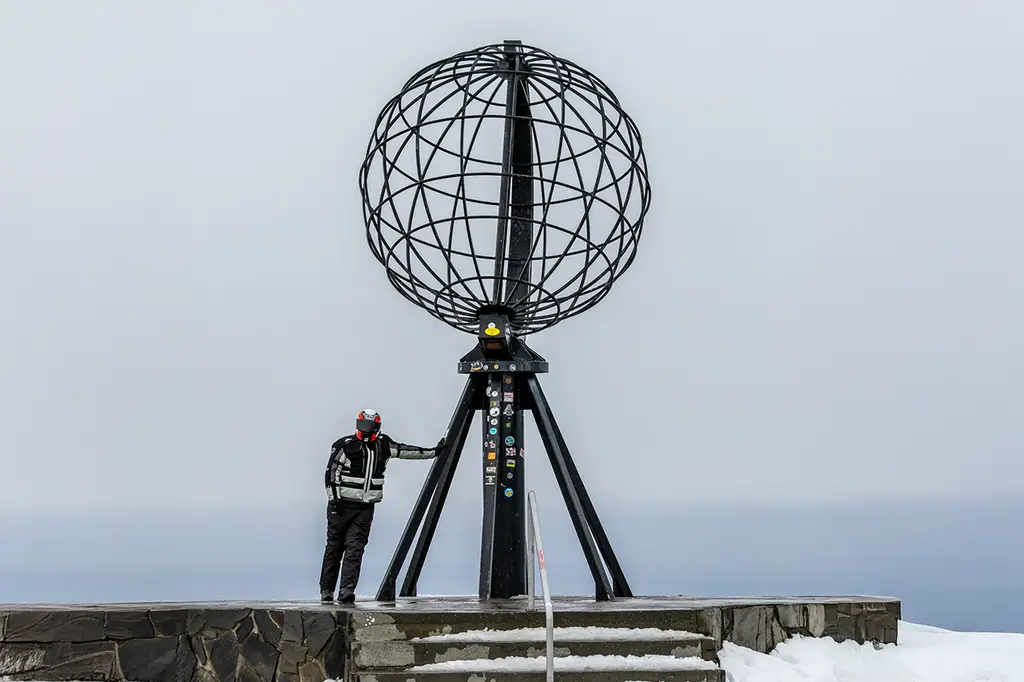 Rider next to a monument at the North Cape after completing the snowy journey on the Versys 1100 with Bridgestone T33 tyres.