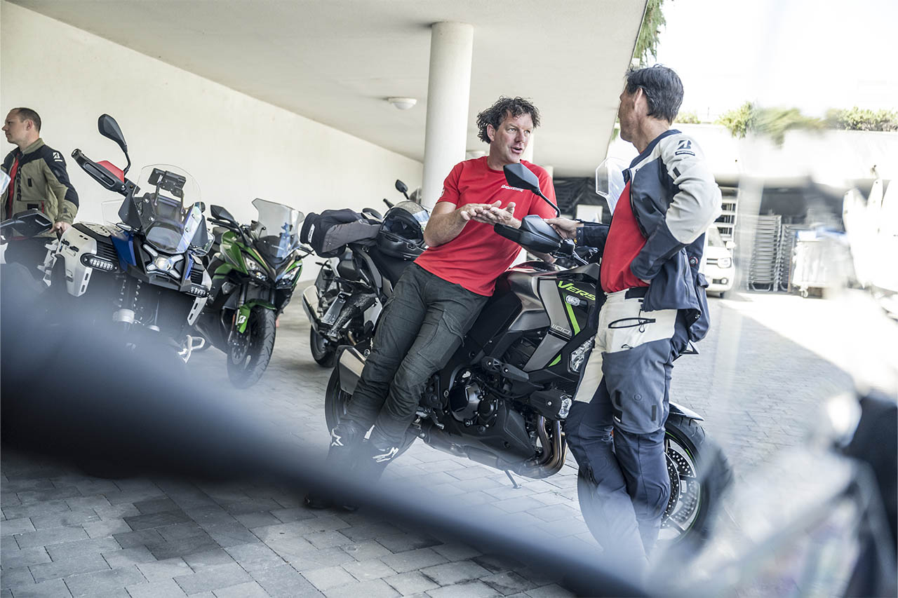 A Bridgestone team member discusses the T33 tyre with a rider beside parked motorcycles 