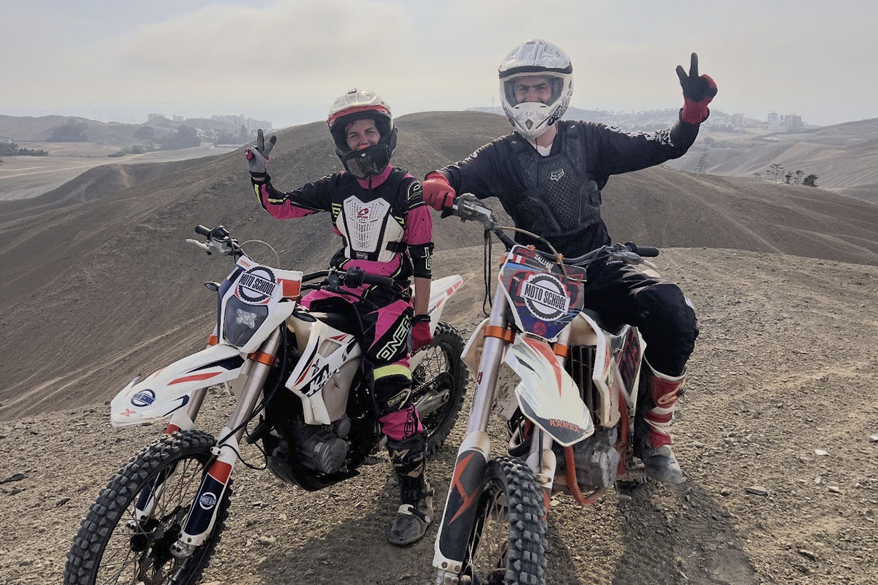 Two riders posing on dirt bikes on a dusty hillside during a guided ride