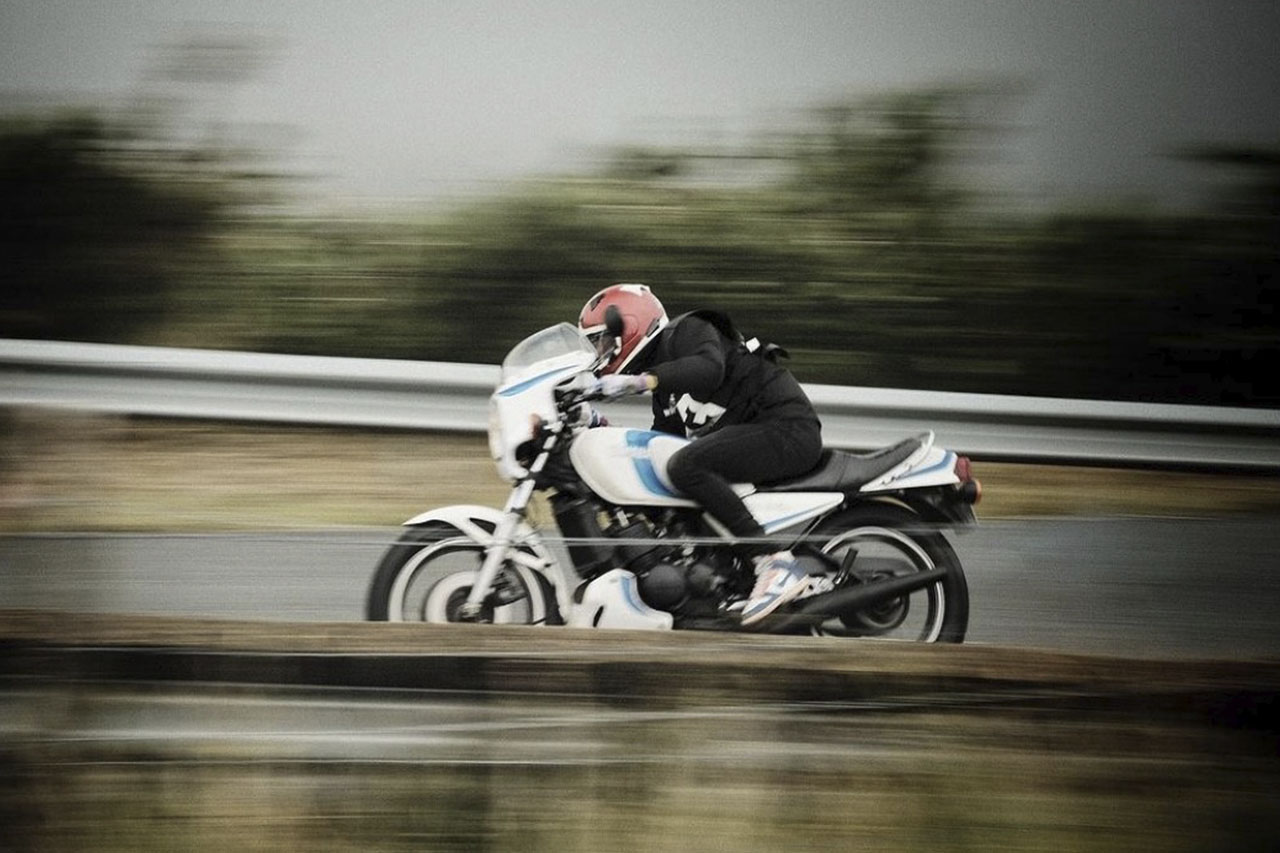 A rider leaning into a corner on a vintage motorcycle on a wet road