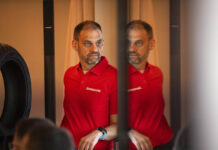 Bridgestone Behind the Scenes: A Conversation with Dominique Plom, Product & Key Account Manager Dominique Plom, wearing a red Bridgestone polo shirt, reflected in a mirrored panel beside a motorcycle tyre.