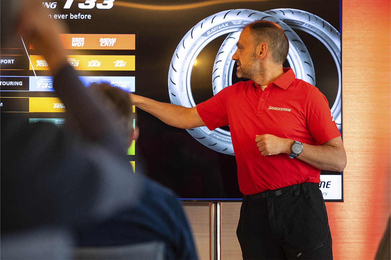 Dominique Plom presenting Bridgestone's Battlax tyre range on a screen to a seated audience.