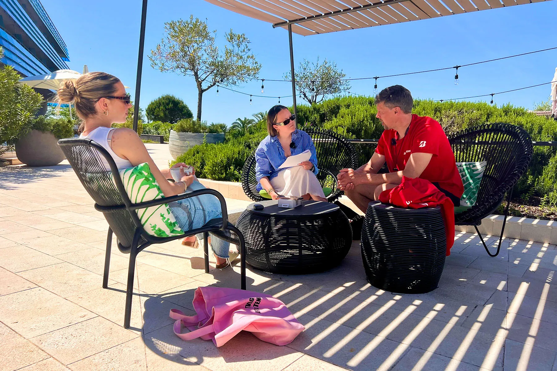 Eric being interviewed by Frauke and Paulien on a sunny terrace with olive trees and string lights