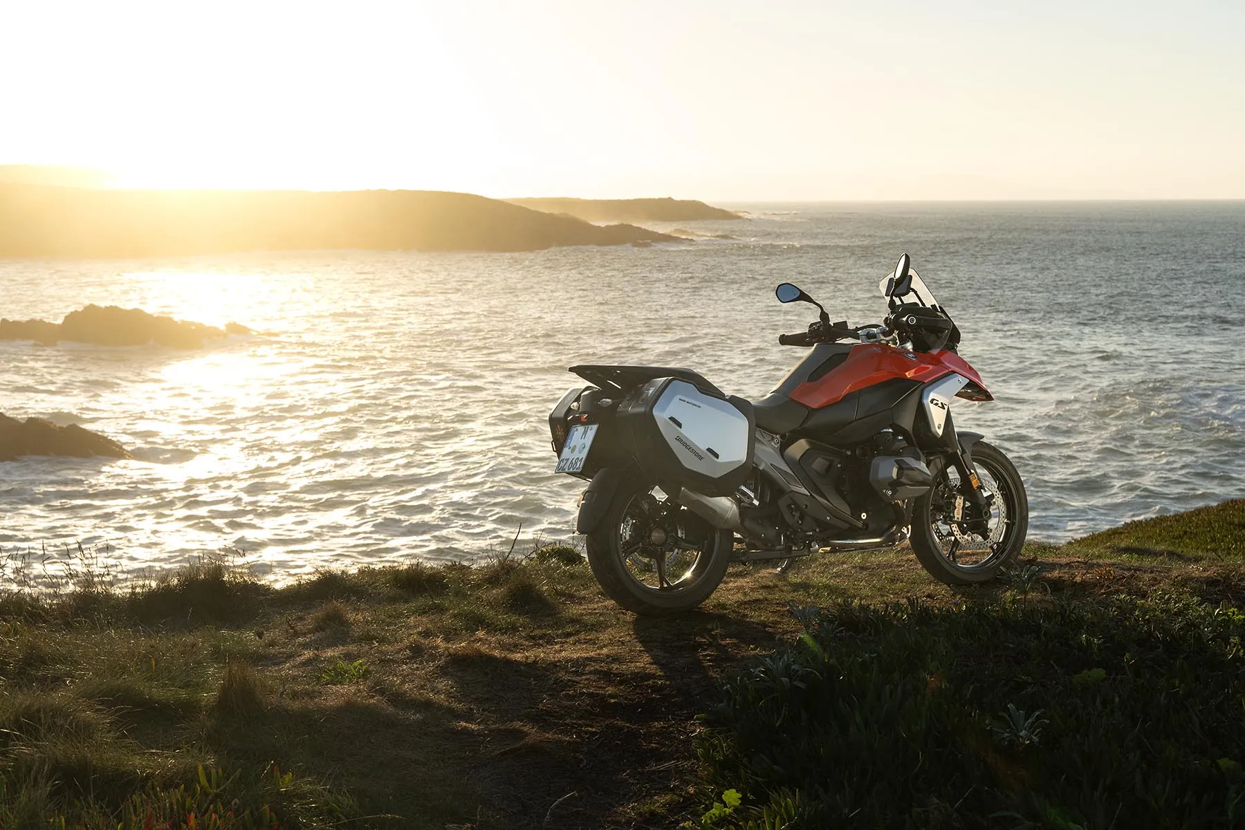 Adventure motorcycle with panniers parked on a coastal cliff at sunset, fitted with Bridgestone Battlax Adventure A42 tyres