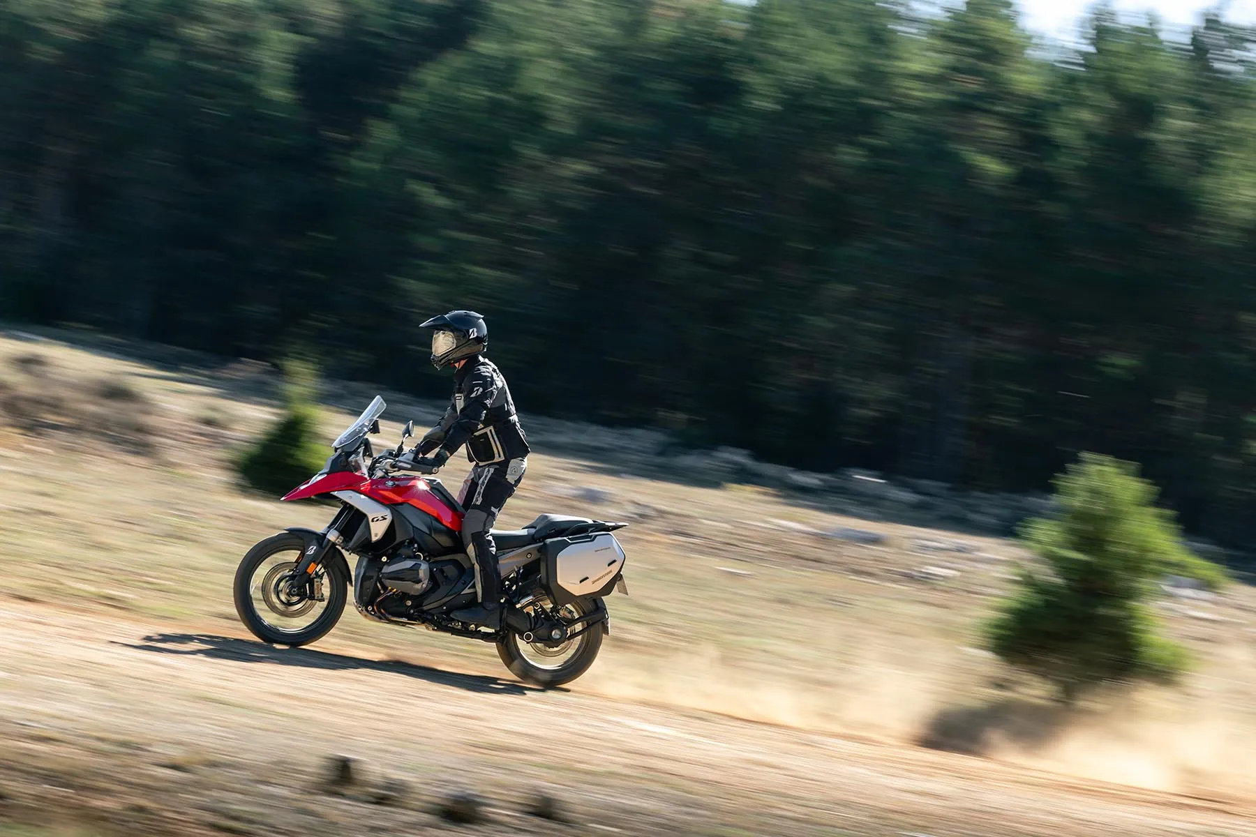 Rider on an adventure motorcycle with Bridgestone Battlax Adventure A42 tyres on a gravel trail through a pine forest